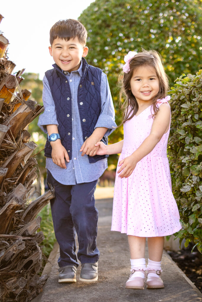 Young siblings smiling and holding hands in coordinating outfits during golden hour family session in the San Francisco Peninsula.