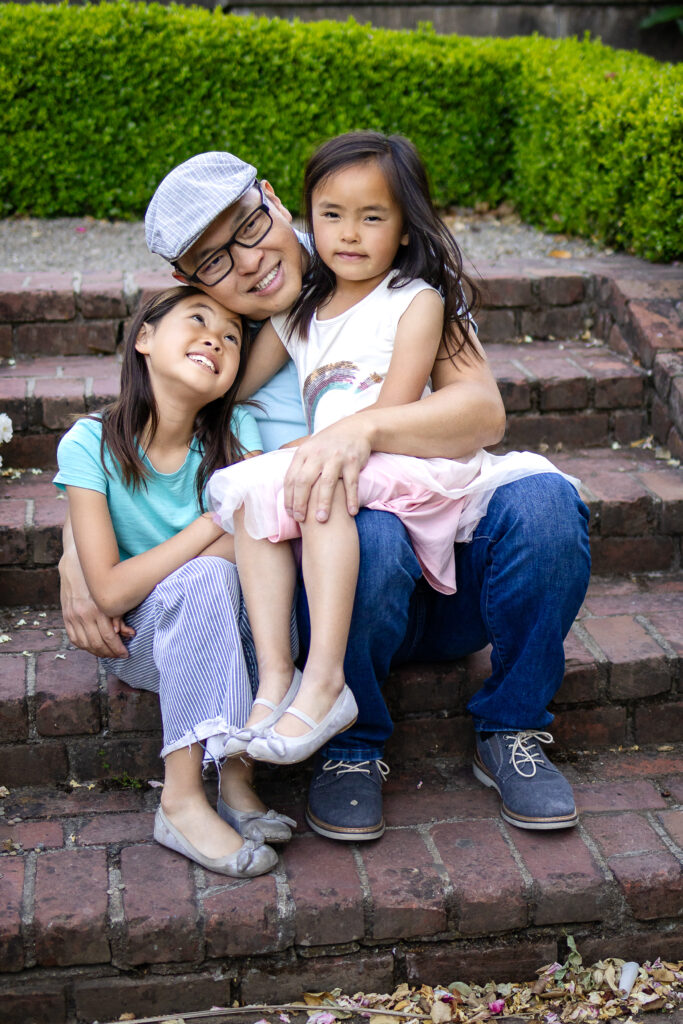 Dad sitting on brick steps cuddling with his two daughters at Kohl Mansion Burlingame