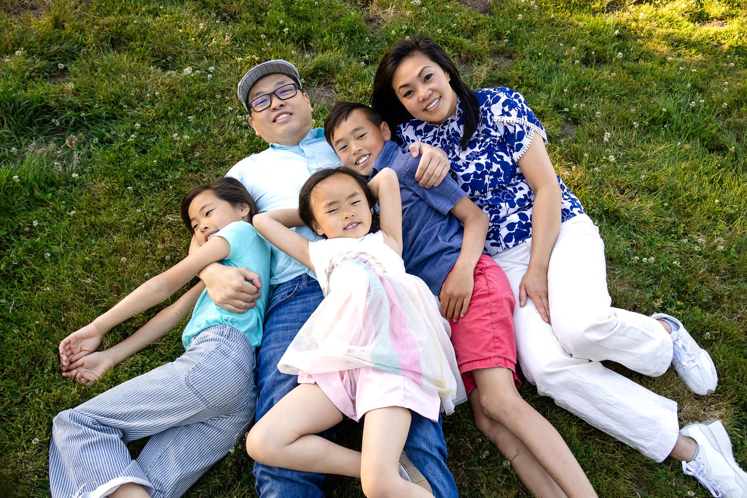 Family of five lying on green grass in relaxed group hug at Kohl Mansion Burlingame