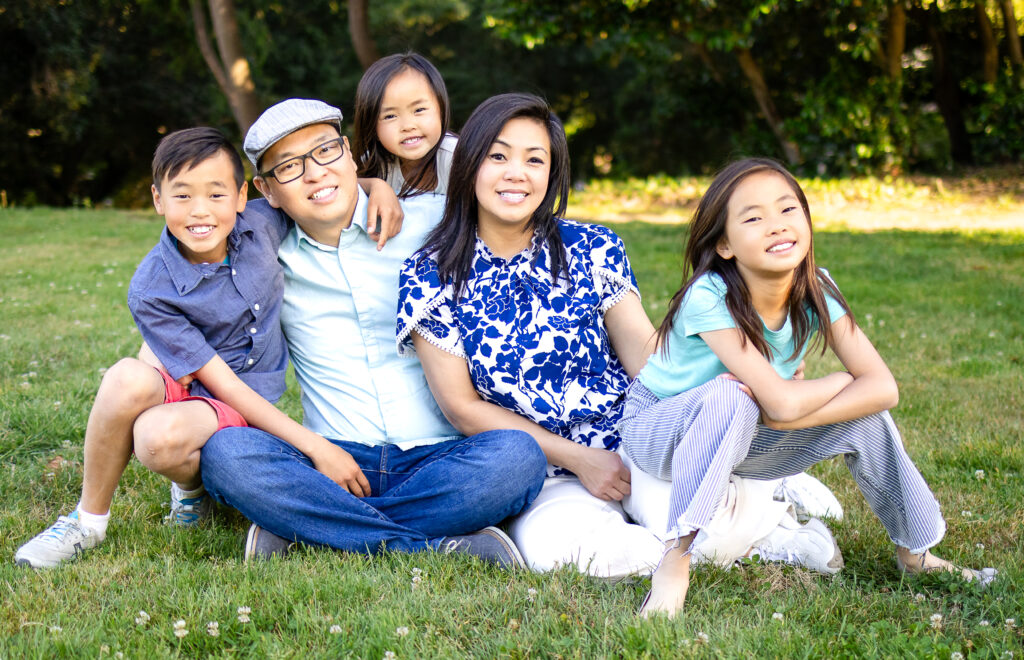 Lifestyle photo of family sitting in the grass, capturing relaxed smiles and sibling closeness at Kohl Mansion Burlingame