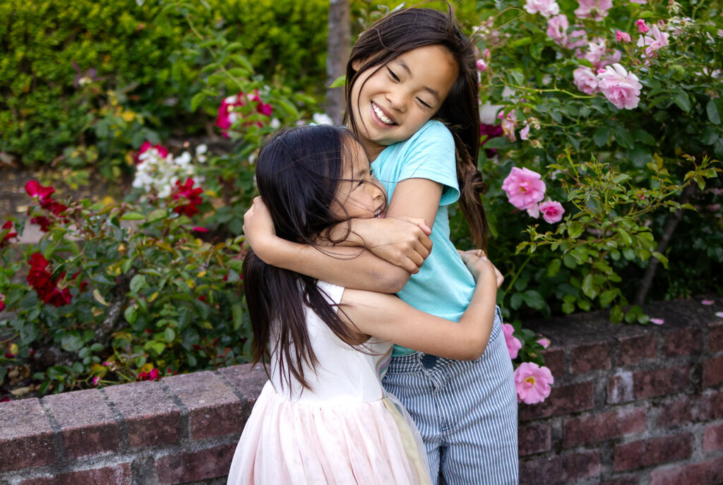 two sisters sharing a sweet moment beside white roses