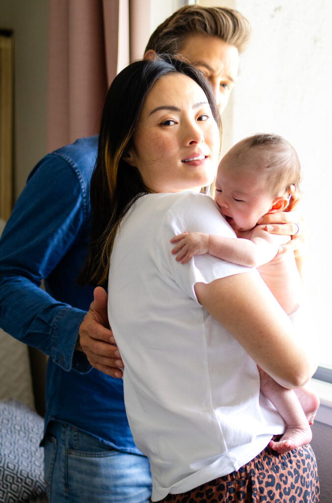 Parents embracing their newborn near the nursery window with natural light
