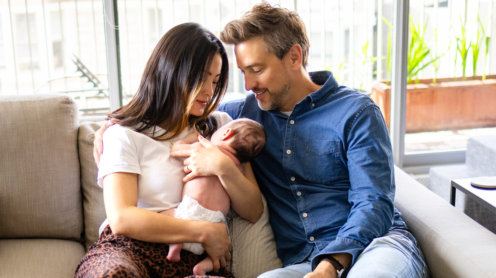 Newborn Lifestyle Photography session of parents seated on the nursery floor smiling at their baby cradled in dad’s arms