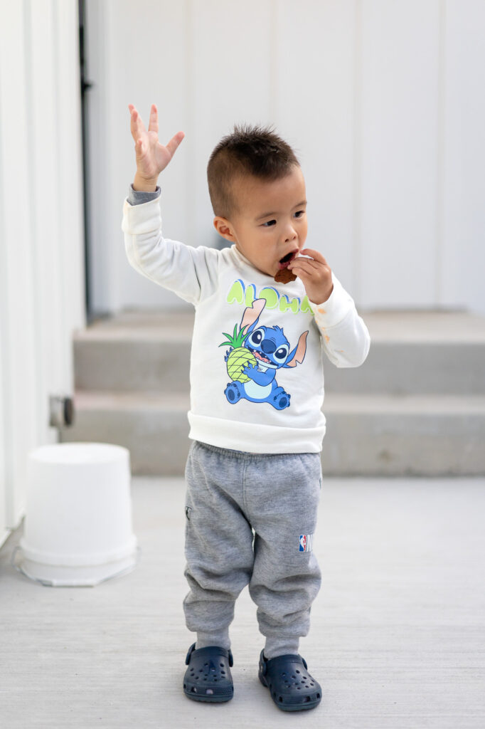 oddler raising hand and eating a cookie outdoors in comfy clothes – Tips for Family Photos with Toddlers - ellobelle photography