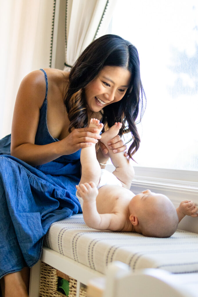 Mom laughing while gently holding her baby’s feet, capturing the joy of early motherhood during ideal time for newborn photos