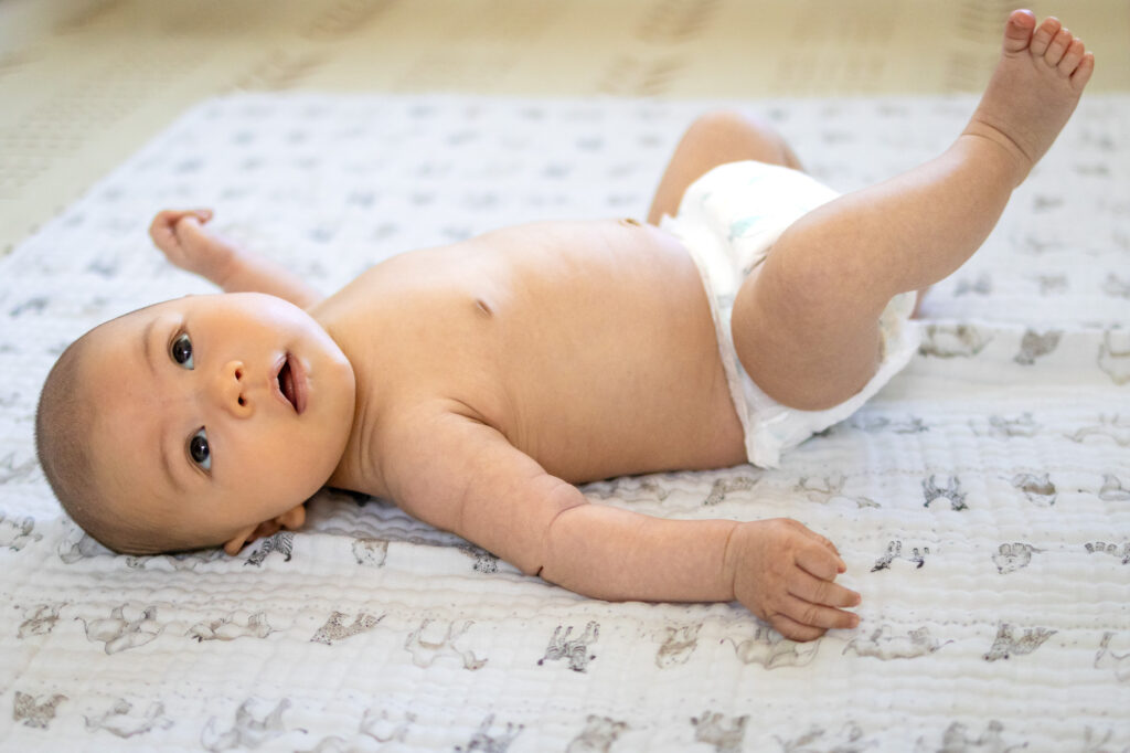 Baby in diaper lying on back with legs raised on patterned blanket for a ideal window for relaxed newborn photos article