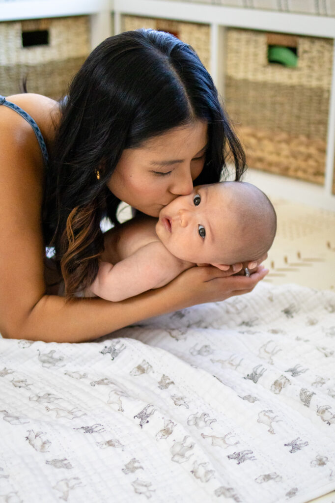 Mom gently kissing her baby while lying down together for a when to book an in home newborn session feature