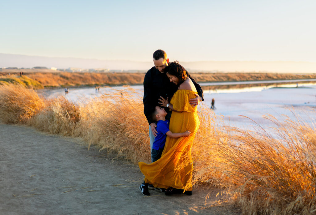 Parents and young son share a warm hug surrounded by golden grass at Alviso Marina County Park – Ellobelle Photography