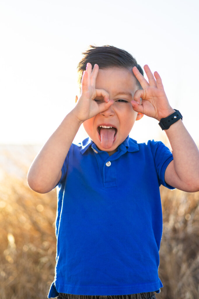 Young boy makes playful hand gestures and silly face during sunset at Alviso Marina County Park – Ellobelle Photography