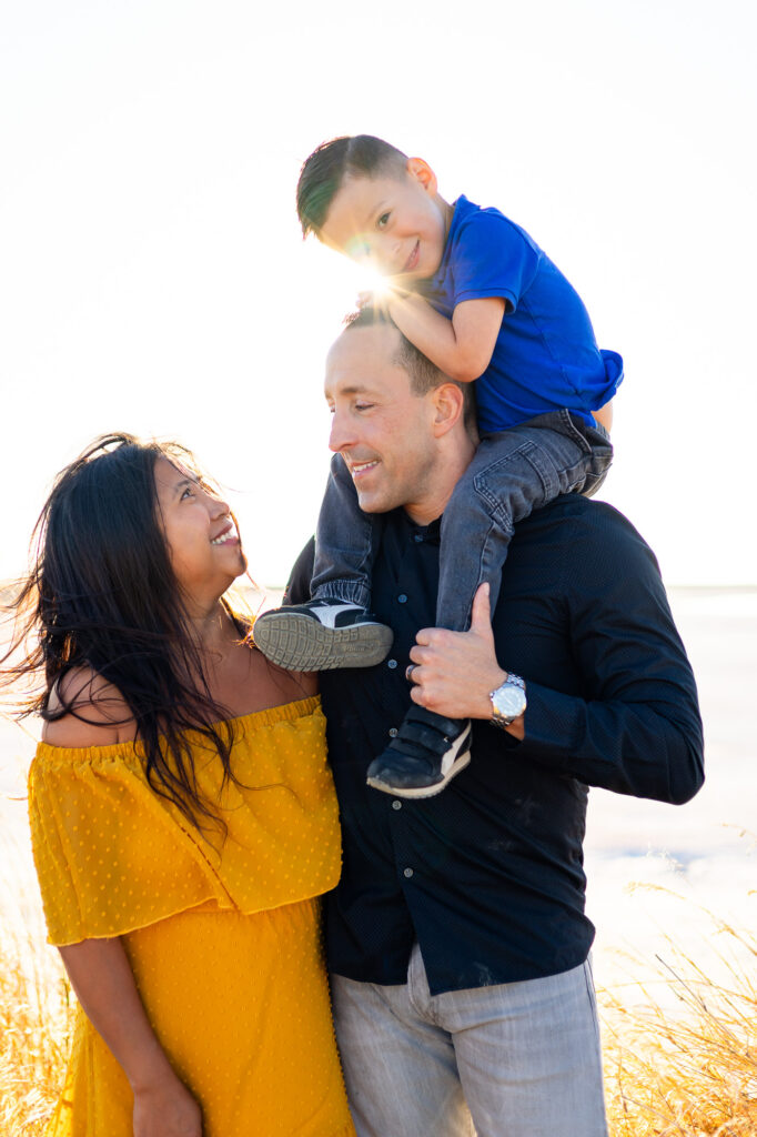 A joyful family shares a golden hour moment with their son on dad’s shoulders at Alviso Marina County Park – Ellobelle Photography