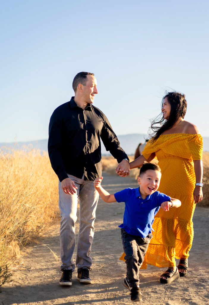 Young boy runs ahead joyfully while holding hands with his parents at Alviso Marina County Park – Ellobelle Photography