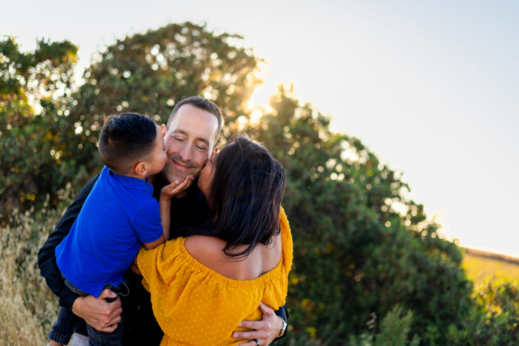 Mom and son kiss dad on both cheeks with laughter and love at Alviso Marina County Park – Ellobelle Photography