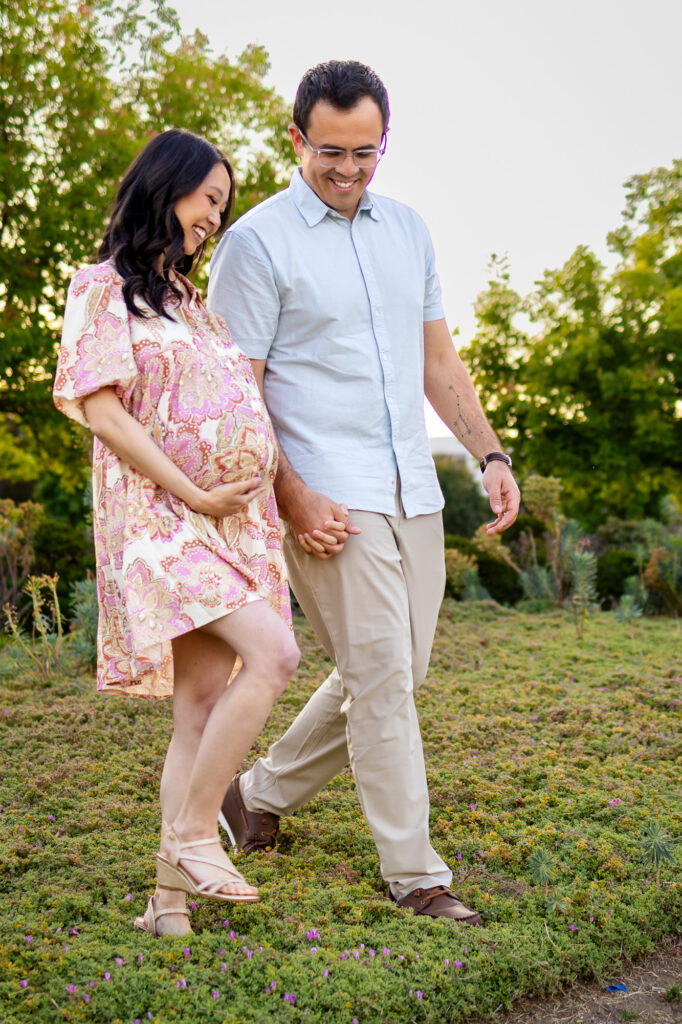 Partner holding mom-to-be’s hand as they walk across a grassy field during sunset
