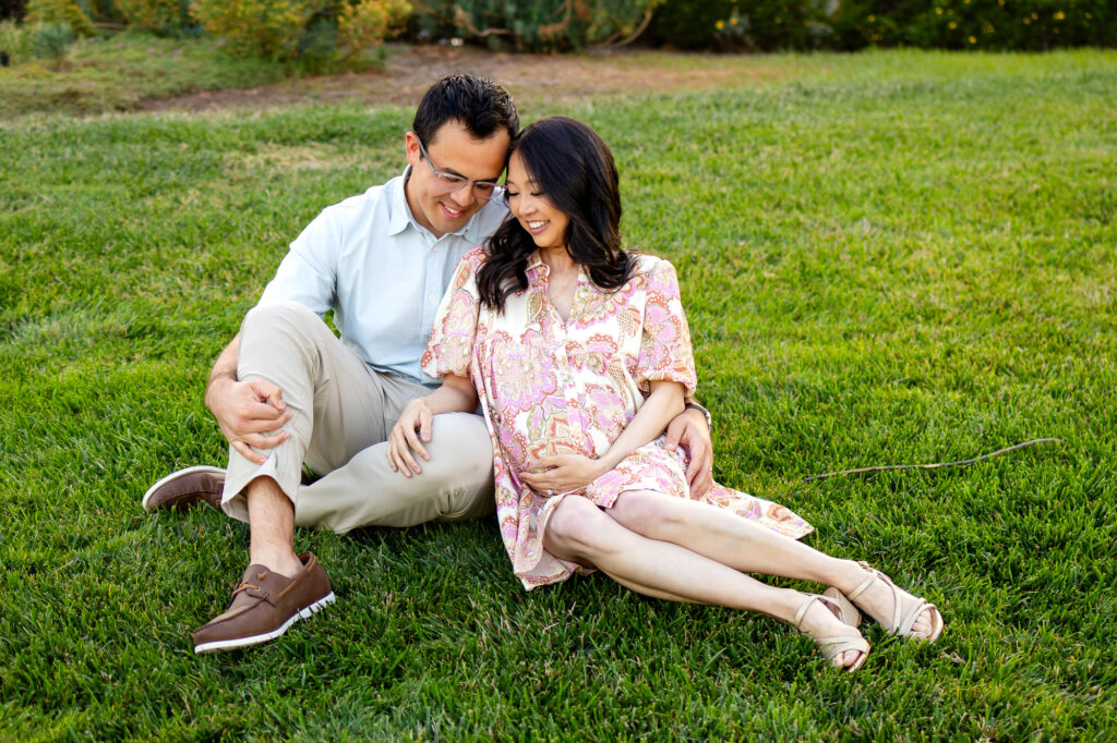 Pregnant woman cuddles partner on dock with view of water behind them