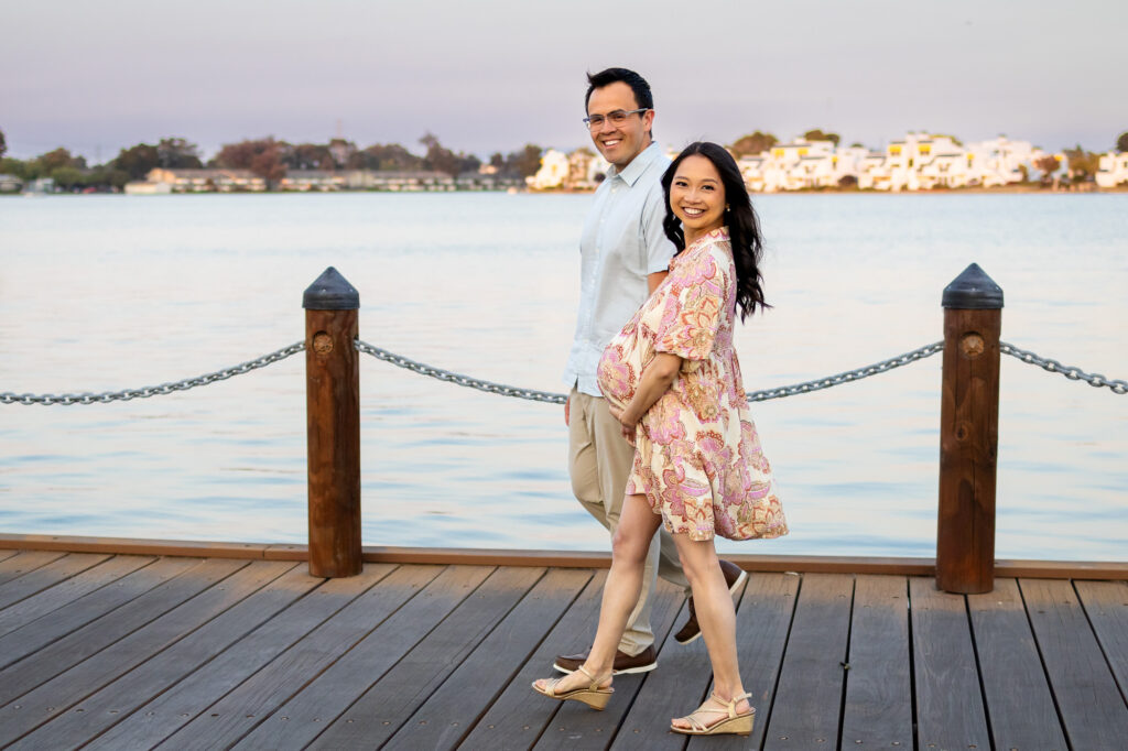 Couple walking hand in hand on dock during maternity shoot at golden hour