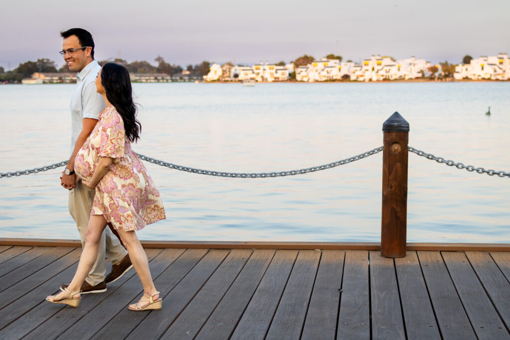 Expecting couple walking along a peaceful lakeside boardwalk, holding hands and enjoying the moment