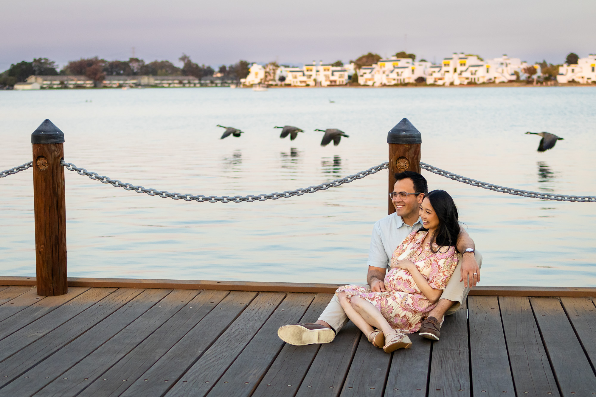 Maternity Photography Poses - ellobelle photography: couple sitting on the dock, holding the baby bump while geese fly behind them