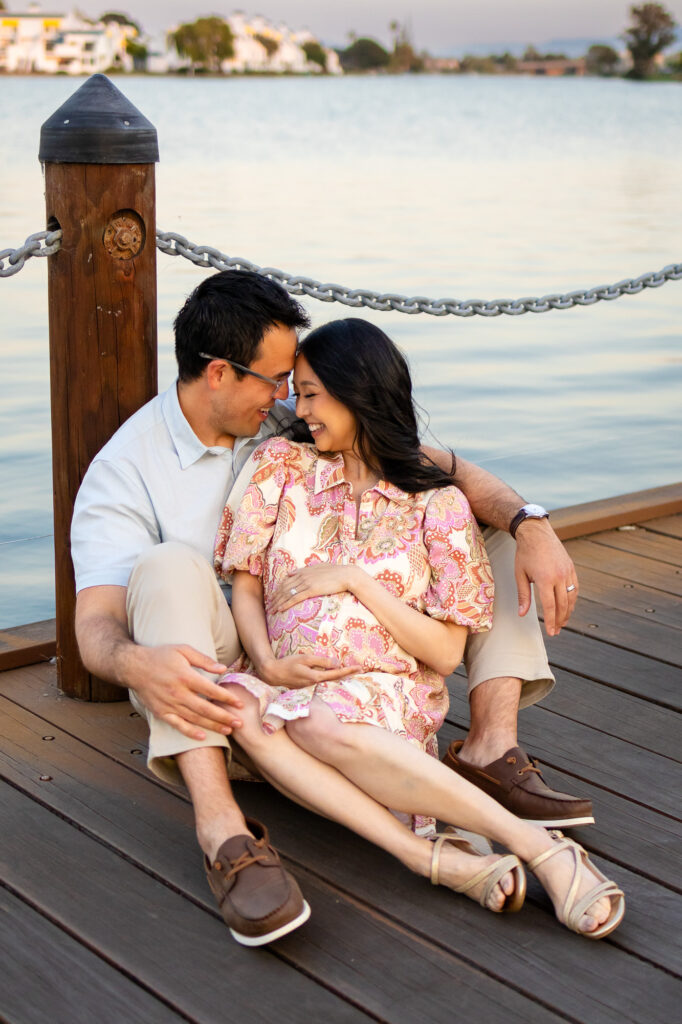 Couple laughing and embracing during a relaxed maternity photo session on a wooden dock
