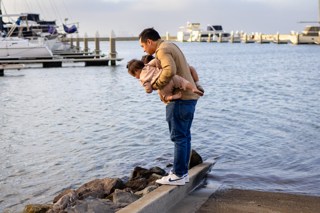Father holding two toddlers exploring at the Oyster Point Marina