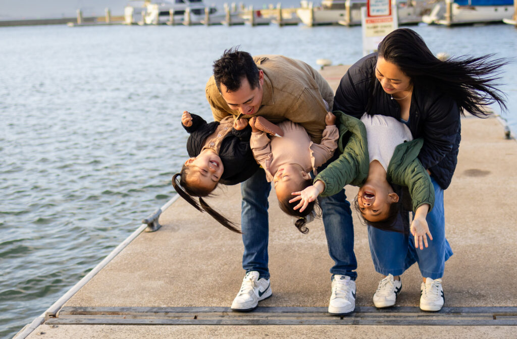 Sweet, playful family moment with parents lifting toddlers near the water at Oyster Point Marina