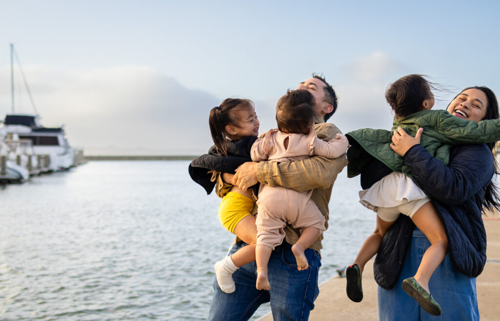 Parents holding children in the air at golden hour near the Oyster Point Marina fishing pier