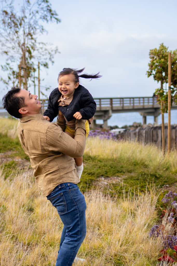 Dad holding daughter mid-spin with fishing pier in the background at South San Francisco waterfront