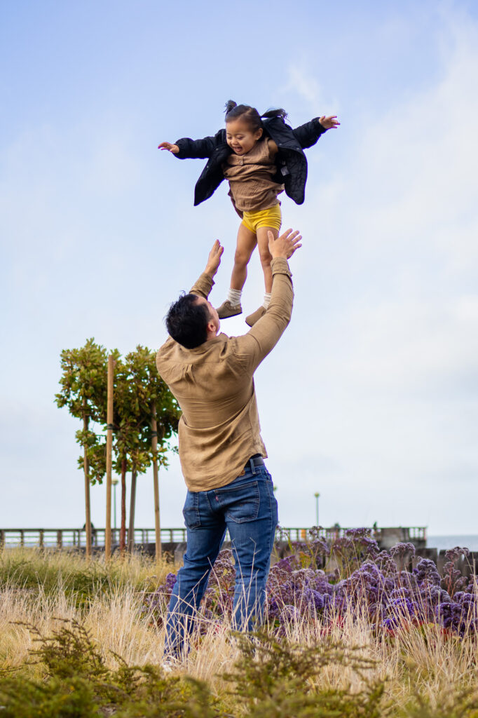 Father tossing daughter into the air surrounded by golden grass and coastal views at South San Francisco Oyster Point