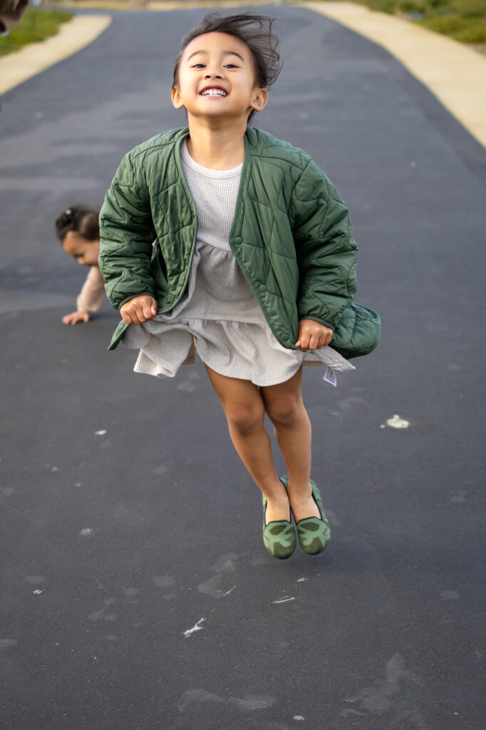 Little girl mid-jump with windblown hair and bright smile at South San Francisco Oyster Point - Ellobelle Photography