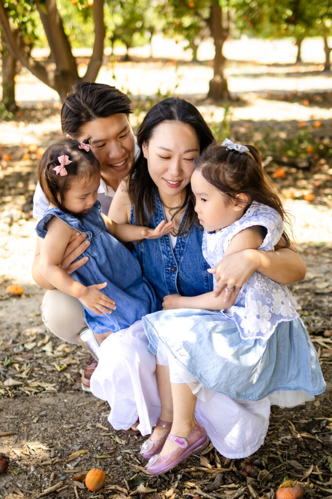 Family crouched close together, smiling with daughters in lap and arms