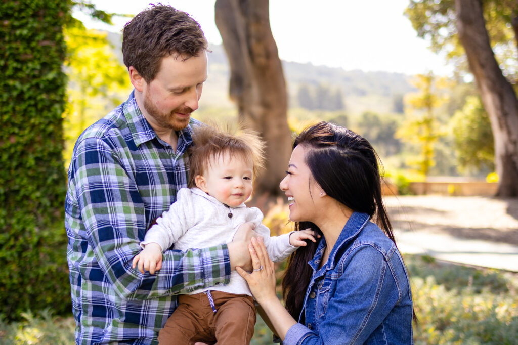 What to Wear for Family Photoshoot - shows loving parents smiling at their baby in sunlit nature setting.
