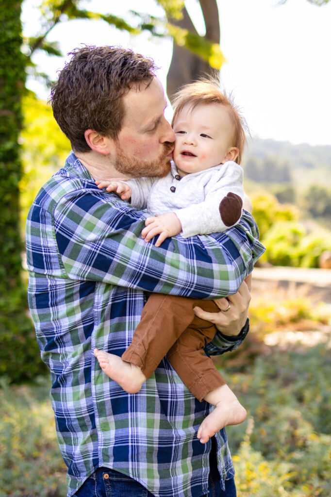 What to Wear for Family Photoshoot - sweet father-son kiss with baby cradled in dad’s arms in Fall Family Outfit