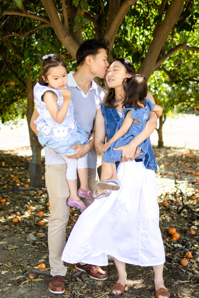 Dad kisses mom’s forehead while holding daughters during golden hour – What to Wear for Family Photoshoot