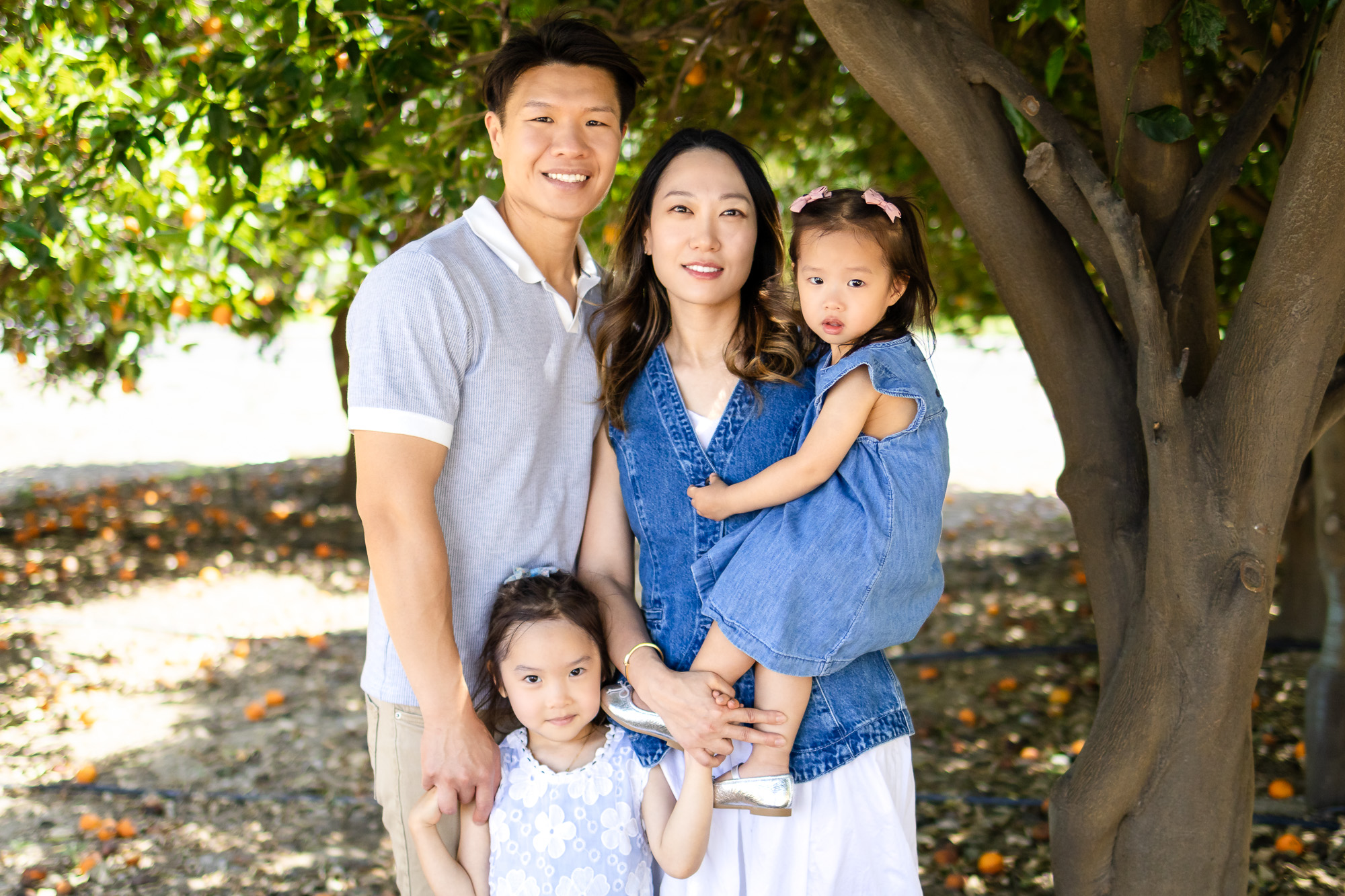 Family of four posed under orange tree, dressed in coordinated neutrals and denim