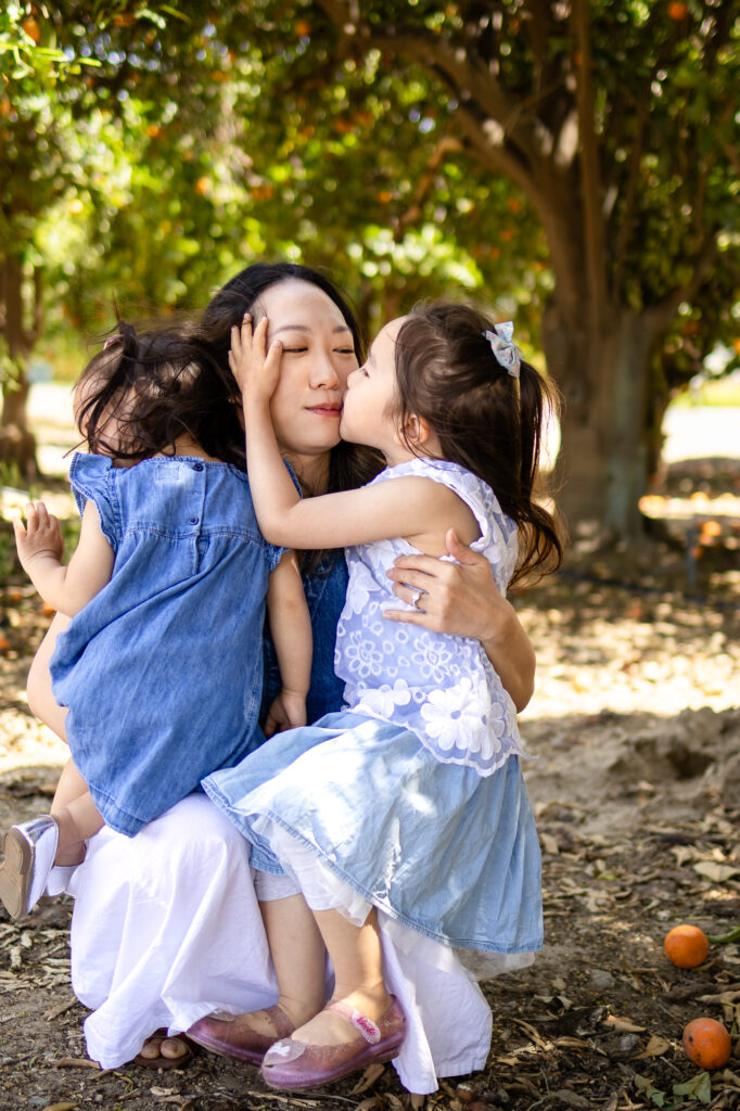 Close-up of mom getting a kiss from daughter while holding both girls – What to Wear for Family Photoshoot