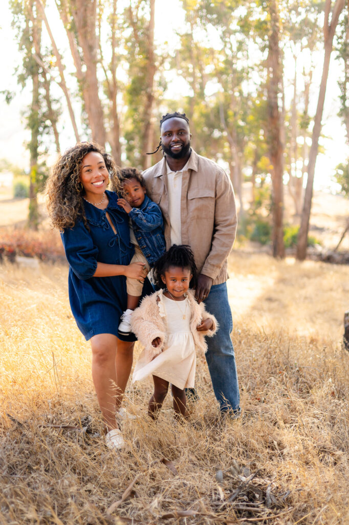 Smiling family standing together in golden field at Coyote Point – Ellobelle Photography