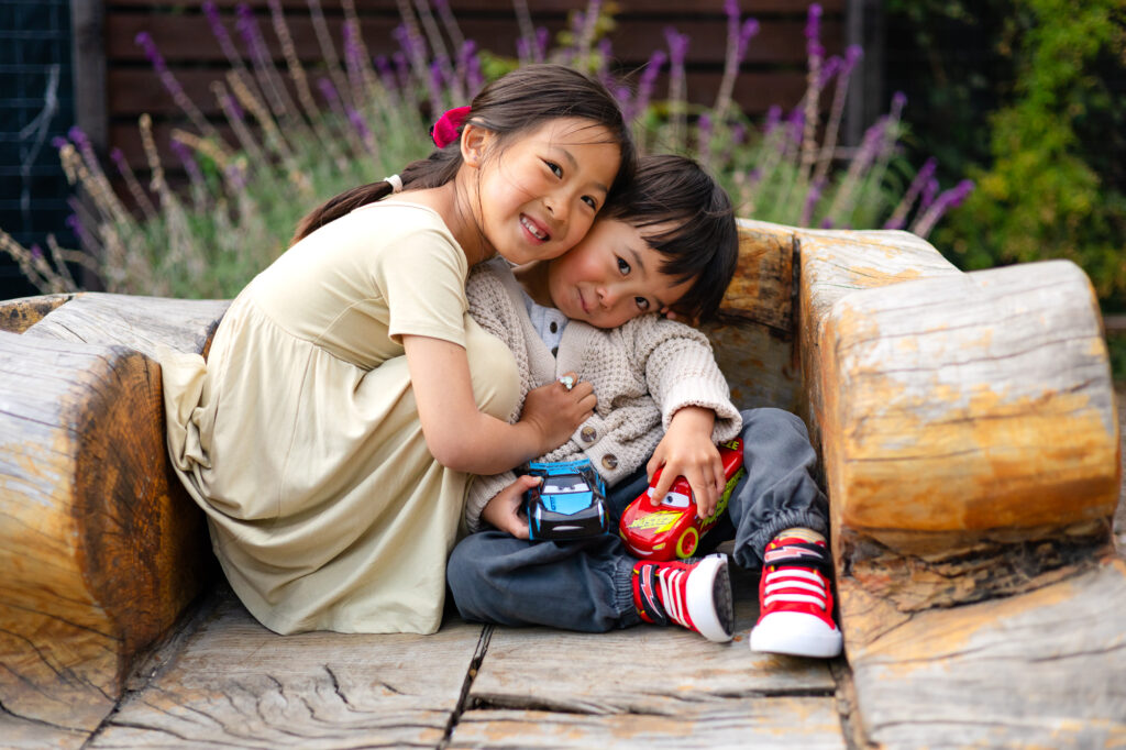 Mini Sessions Photography - Ellobelle Photography: Siblings cuddling with toy cars on a wooden bench