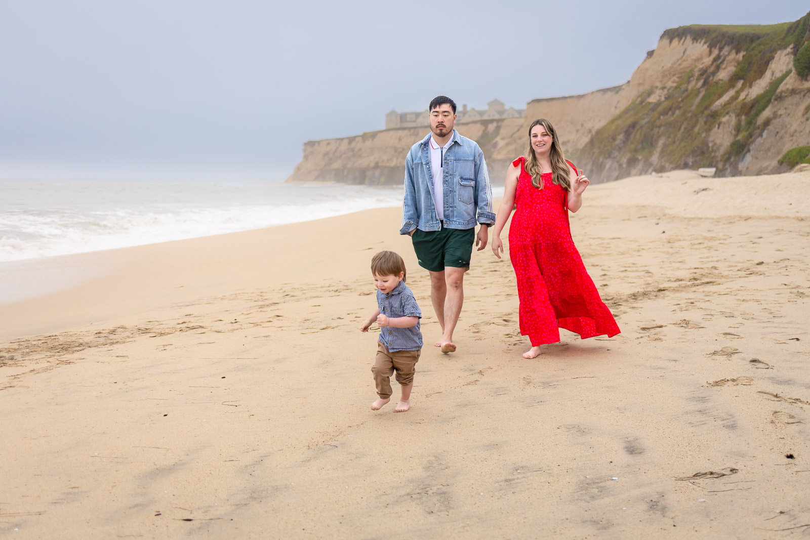 A family walks together along a foggy Half Moon Bay beach during a mini sessions photography session, with dramatic coastal cliffs in the background.