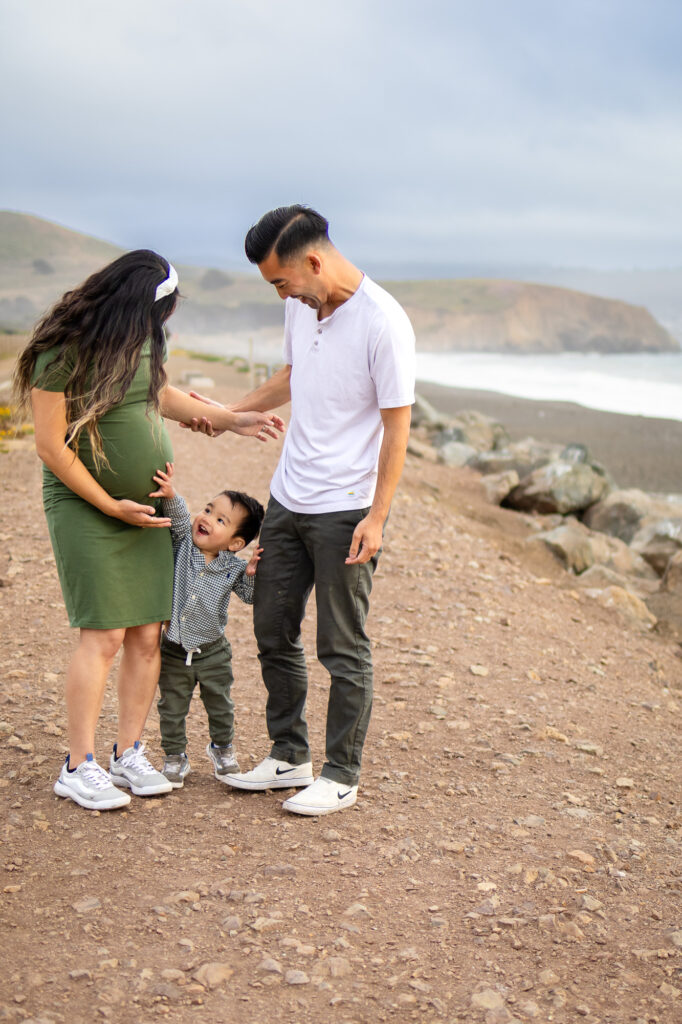 Family laughing together during maternity session on a coastal trail, filled with love and movement.