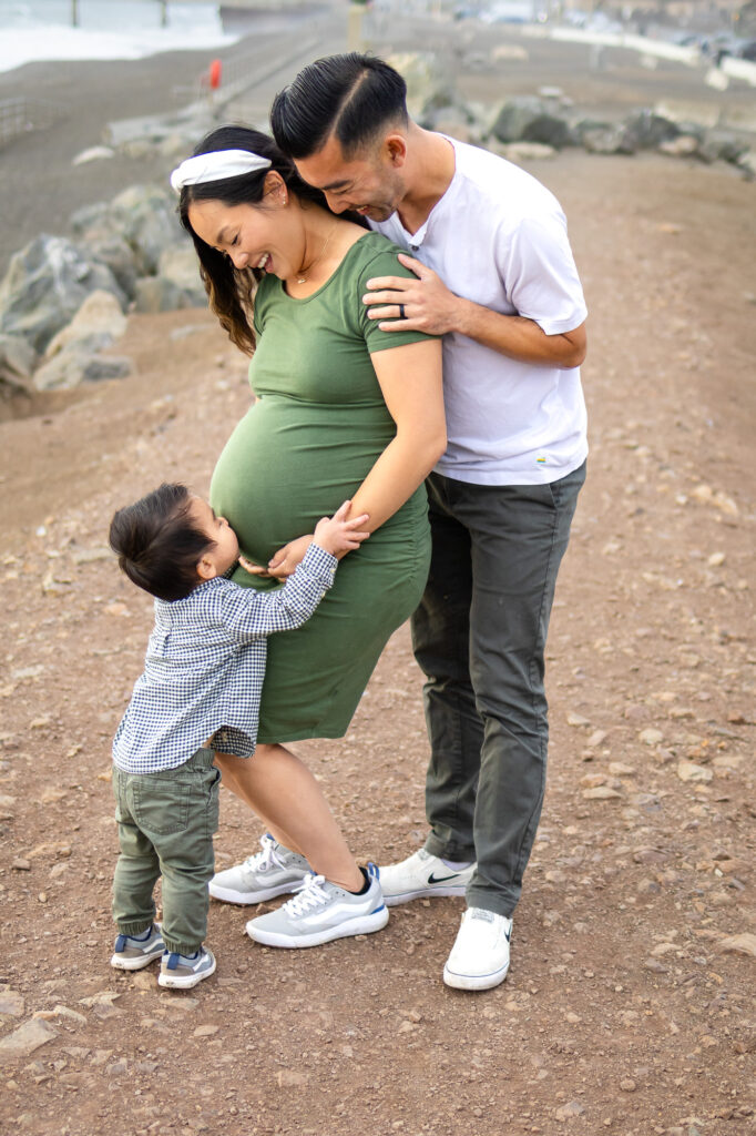 Big brother hugging baby bump while both parents smile with joy.