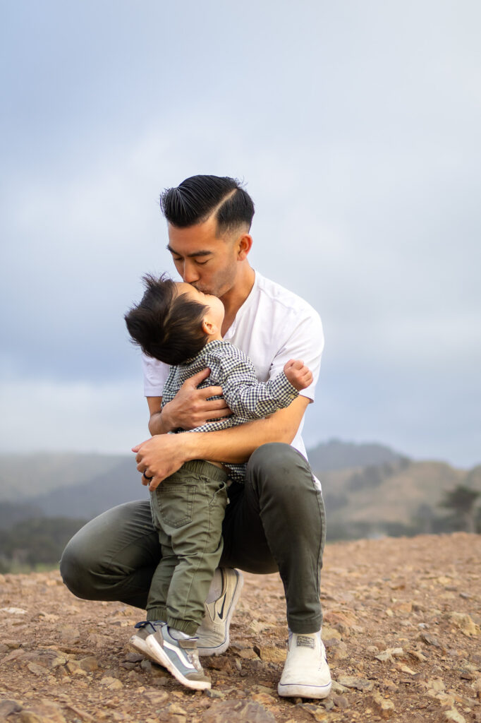 Sweet kiss from dad to mom on the windswept coast — a perfect image from the best time for maternity photos.