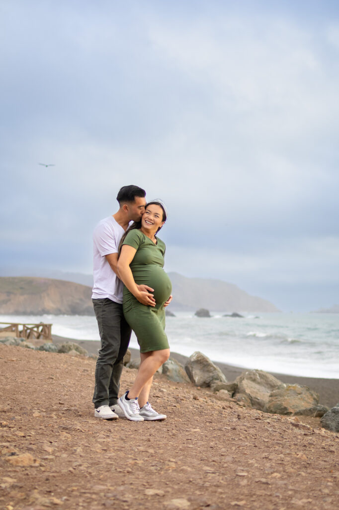 Tender moment between expecting couple, capturing coastal wind and love.