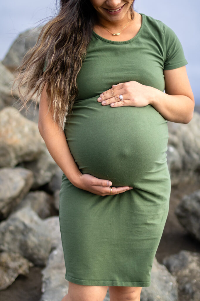 Close-up of expecting mom’s hands cradling her belly during a lifestyle maternity shoot on the coast.