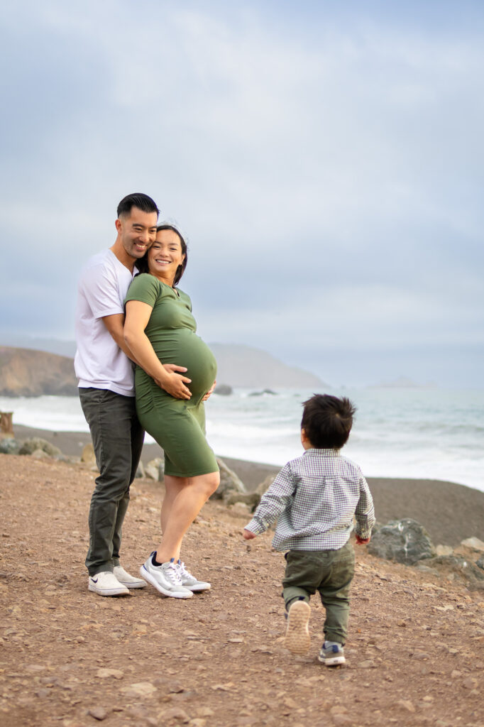 Playful maternity moment with couple embracing as the tide rolls in behind them.