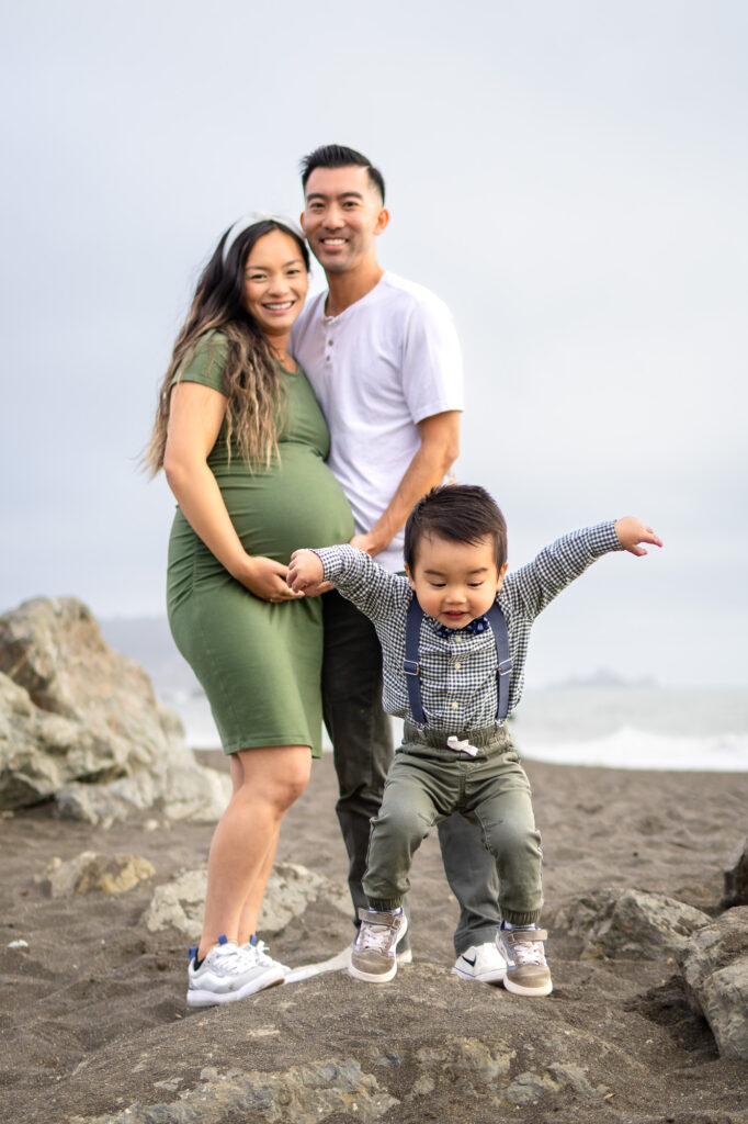 Family smiling as toddler leaps forward during a relaxed, joyful maternity photo session.