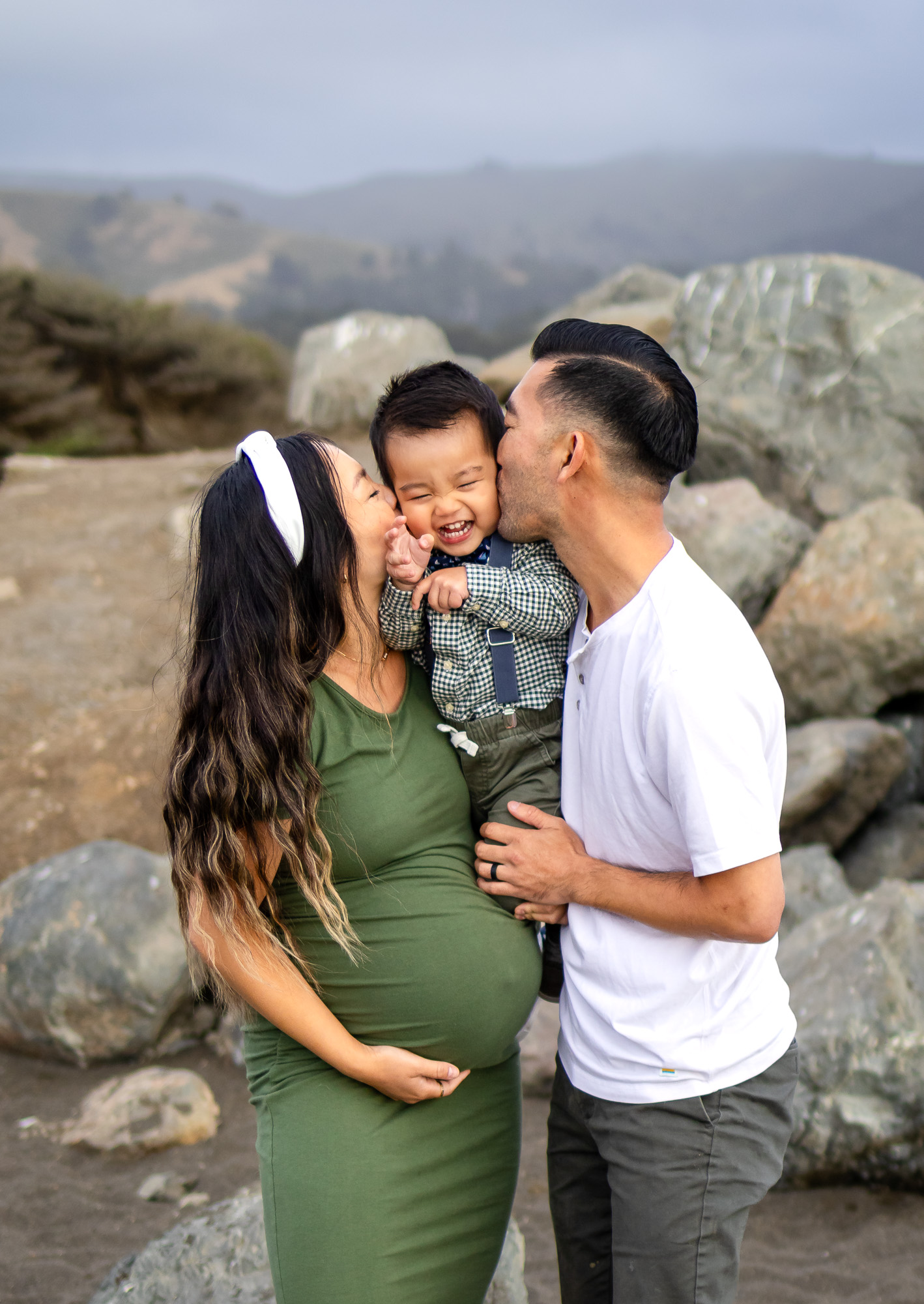 Parents kissing giggling toddler while expecting mom cradles her belly—capturing the best time for maternity photos.