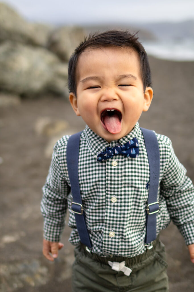 Toddler sticking out tongue during a fun, candid family maternity session on the beach.