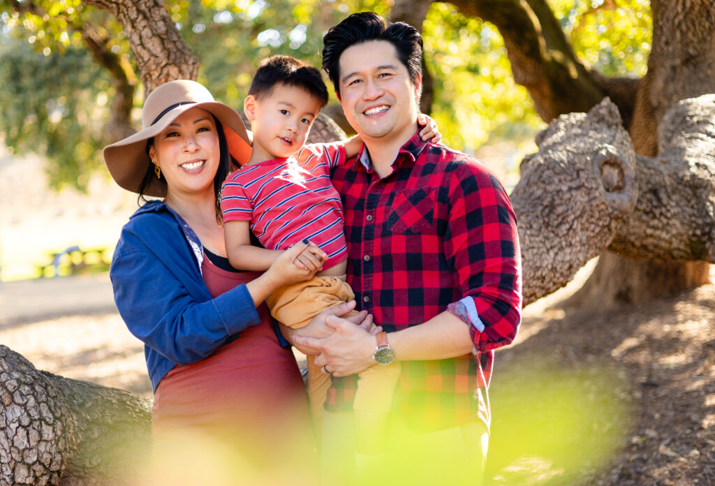 Parents smiling with their child in front of oak trees at Laurelwood open space