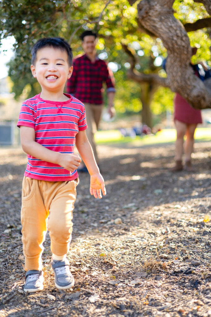 Young boy smiling and running during family photos along the hillside trail in San Mateo