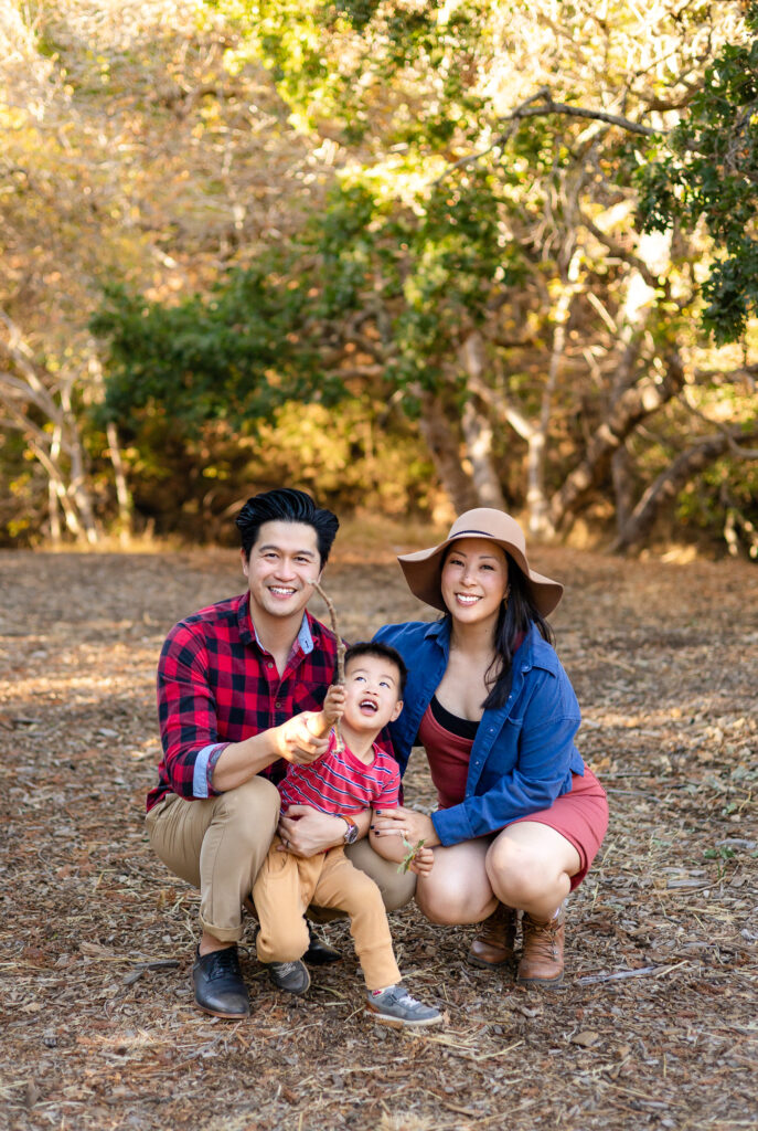 Family crouching together and smiling outdoors at park with scenic views