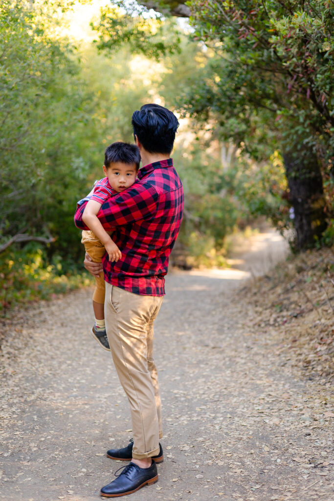Dad holding young son while walking on a shaded trail